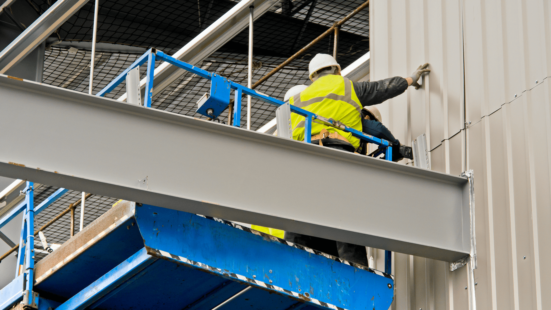 workers in vets and hard hats adding cladding to a building