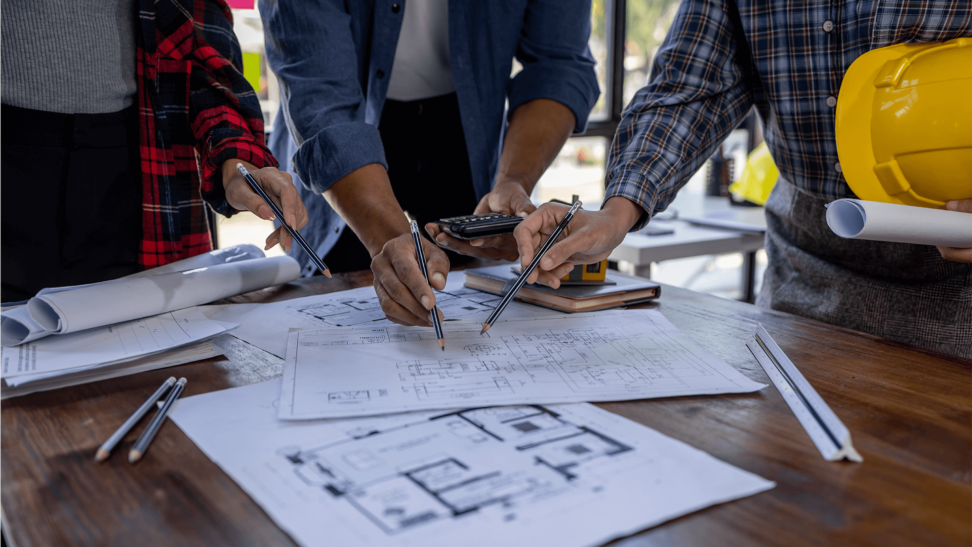 three commercial architects looking at several blueprints on a desk